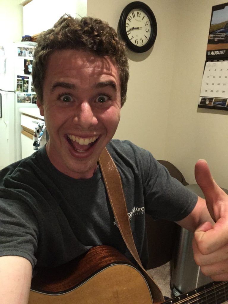 Joel smiling and giving a thumbs-up with a guitar